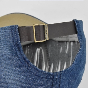 Dettaglio macro del cappellino in denim lavato con cinturino in pelle e fibbia in bronzo