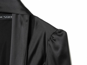 Detailed close-up of glossy black satin shirt neckline with elegant stitching and label