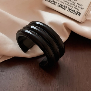 Detailed view of a black three-layer geometric resin cuff bracelet on a wooden surface