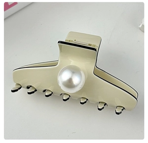 Macro shot of an elegant cream and black hair claw clip with a large central pearl detail