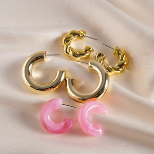 Detailed shot of gold twisted hoops and pink marble acrylic earrings on silk