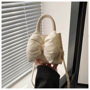 Close-up of off-white crossbody bag featuring a large decorative bow and soft PU texture