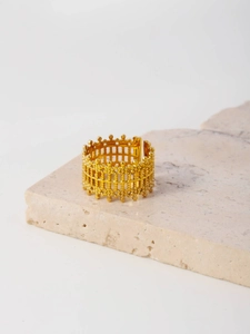 Macro detail of golden crown mesh ring with beaded texture on minimalist stone surface