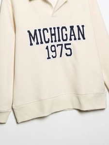 Gros plan sur la broderie Michigan 1975 d'un sweat crème à col polo