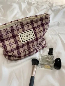 Close-up of a plaid tweed makeup bag in burgundy and beige with a metallic zipper detail
