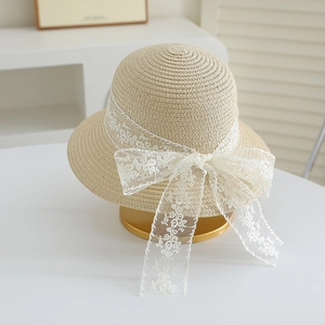Detail of a beige straw hat featuring delicate white floral lace bow and intricate embroidery
