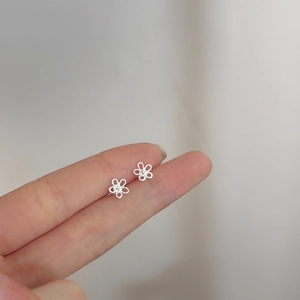 Close-up of minimalist silver hollow flower stud earrings held between fingertips