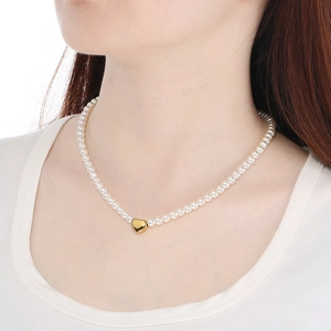 Detail of elegant pearl necklace with gold heart pendant worn on model for scale and fit