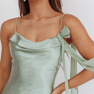 Dettaglio dell'abito in raso verde salvia con scollo a cappuccio e fiocco sulla spalla