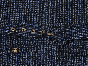Detail van blauwe en zwarte tweed stof met metalen oogjes en knoop op de jurk