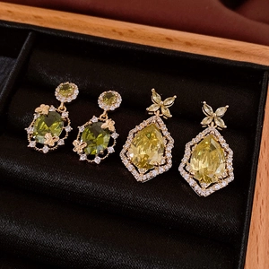 Macro détaillée de boucles d'oreilles fleuries dorées avec zircons verts et jaunes sur velours
