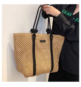 Detail of hollow woven straw tote bag with black rope handles and vertical stripes