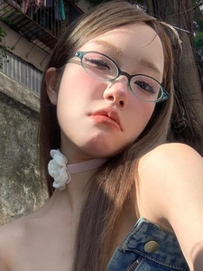 Close-up of model wearing oval teal transparent glasses and a white floral crochet necklace