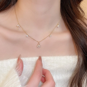 Close-up of gold plated necklace with key, padlock, and pearl charms on a model