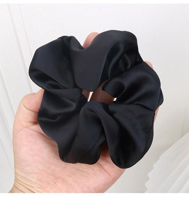 Close-up of oversized black satin scrunchie showing glossy fabric texture and soft pleats