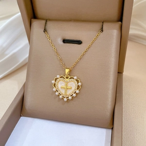 Nahaufnahme goldener Herzanhänger mit Kreuz, Muschelbasis, Diamanten und Perlen auf Seide