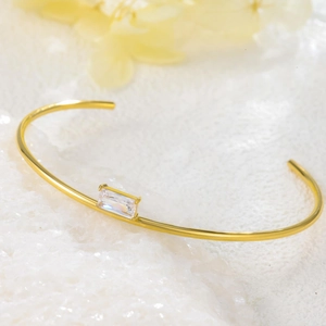 Detail view of a gold-plated titanium steel bangle featuring a baguette-cut zircon stone