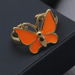 Macro view of adjustable orange enamel butterfly ring with polished gold-plated finish
