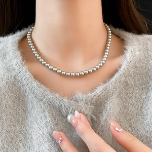 Detail of elegant grey pearl necklace worn by model against soft grey knitwear