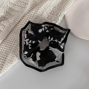 Detailed shot of black and white floral scrunchie with sheer mesh edges on white background