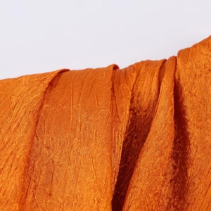 Close-up of bright orange satin fabric showing detailed pleated texture and fine glossy finish