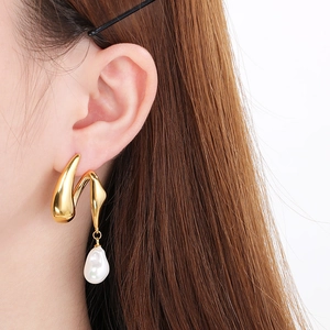 Detail of gold sculptural earring with irregular pearl drop tassel on model