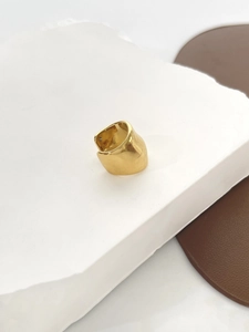 Detail view of a wide polished gold horseshoe-shaped ear cuff on a stone background