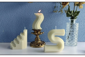 Drie geometrische crème-witte decoratieve kaarsen in trap-, S- en golfvorm met gouden houder