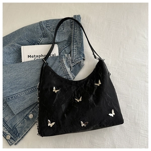 Close-up of black pleated texture shoulder bag with silver butterfly charm on white cloth