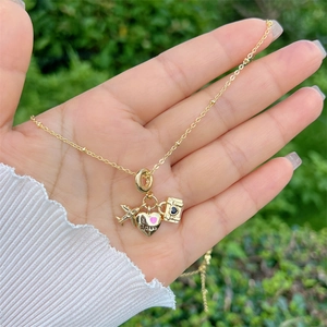 Dettaglio di una collana da viaggio dorata con aereo, ciondolo a cuore e charms valigia