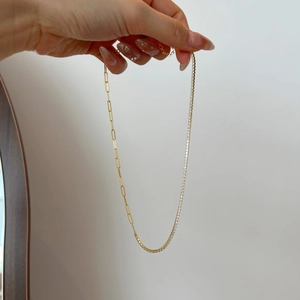 Detail of gold paperclip chain and white zircon tennis chain necklace shown by hand