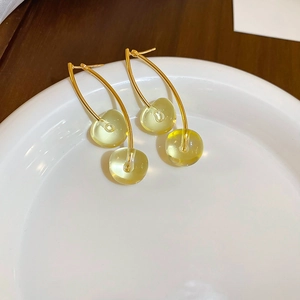 Close-up of translucent yellow-green cherry earrings with gold hooks on a ceramic dish