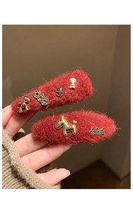 Close-up of red plush hair clips with vintage gold rocking horse and lucky coin charms