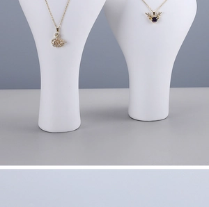 Detail of swan and heart pendants on a white bust jewelry display with gold chains