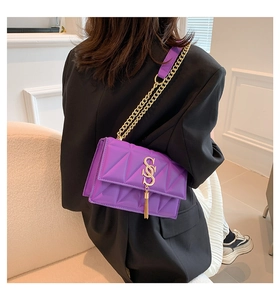 Close-up of purple quilted crossbody bag with gold S-logo buckle and fringe detail