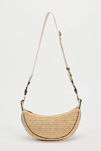 Detail of the woven straw texture and adjustable brown leather strap on the beige bag
