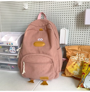 Pink corduroy backpack with cute duck design shown in a cozy study desk setup
