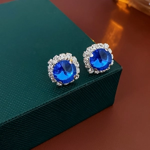 Detailed close-up of blue crystal earrings with white zircon halo on green jewelry box