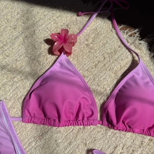 Détail d'un haut de bikini dégradé rose et violet avec une pince à cheveux fleurie