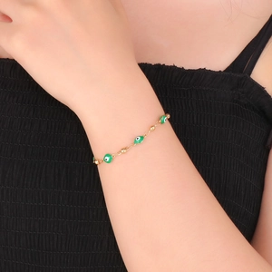 Close-up of a gold chain bracelet with green evil eye charms on a woman's wrist