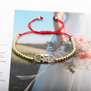 Makro-Detail von rotem Textilarmband mit Sternen-Zirkonia-Anhänger und Goldperlen