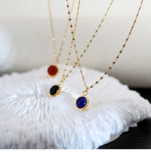 Detailed shot of round natural stone pendants in blue, black, and red on 18K gold chains