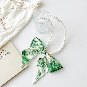 Detail of faux pearl necklace strap with green floral ribbon bow on white tabletop
