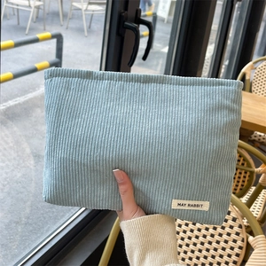 Light blue corduroy makeup bag with vertical texture held in a natural outdoor setting