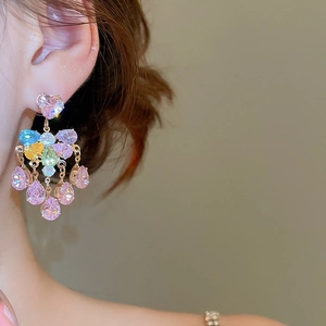 Detailed view of colorful heart and pear-cut gemstone tassel earrings on a model's ear