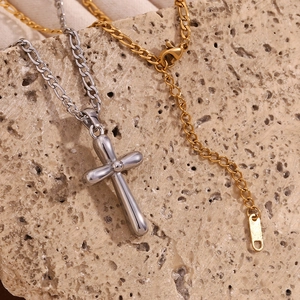 Macro detail of silver cross pendant and golden Figaro chain on beige stone surface