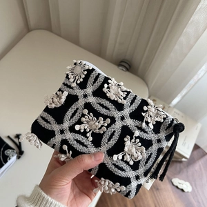 Detail of a mini canvas coin purse featuring black and white floral embroidery and tassels
