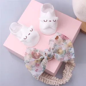 Detail of white knit baby socks with star patch and floral bow headband in a gift box