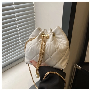 Detailed shot of white quilted bucket bag featuring a gold chain and pearl drawstring charms