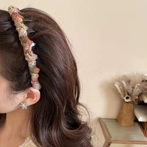 Close-up of a colorful woven tweed headband and silver snowflake stud earring on a model